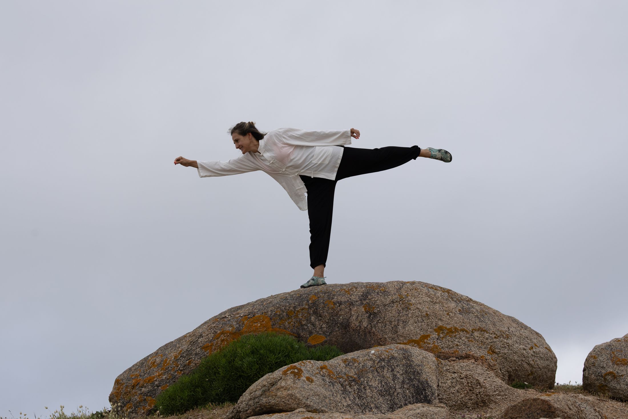 Loly Vázquez en una postura de Tai Chi sobre una roca junto al mar